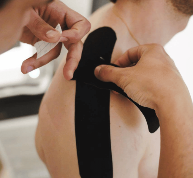 taping kos kiné marseille Gros plan sur un kinésithérapeute entrain de pratiquer du taping sur l'épaule d'un patient